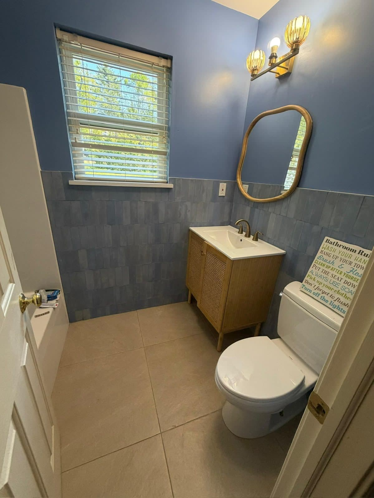 A bathroom with blue walls above a tiled wainscot, timber vanity and a brass-framed mirror