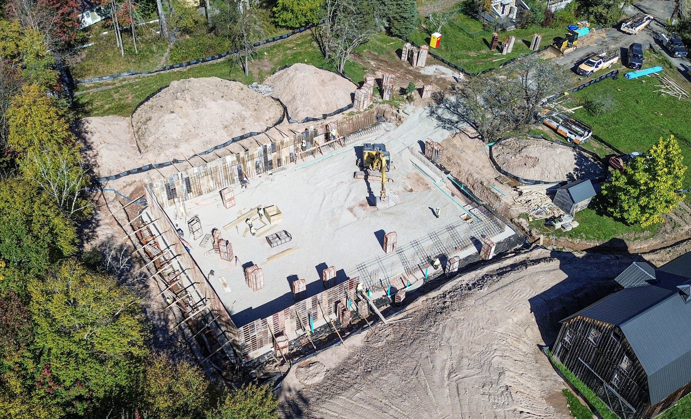 Aerial view of a foundation dug into a wooded lot, spoil heaps either side and the walls formed around a stone base