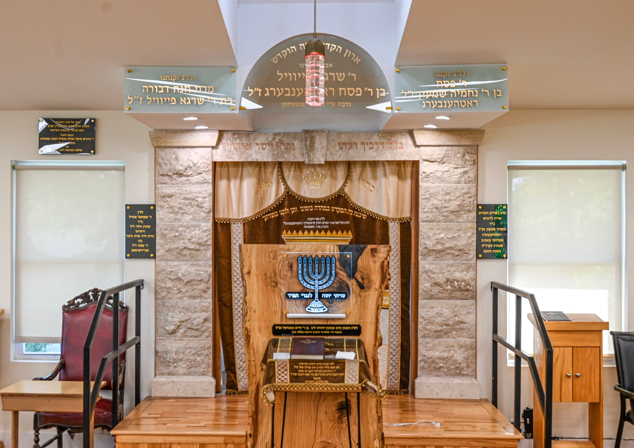An aron kodesh built in as joinery, with a stone-faced surround, curtain and carved doors at the front of the beis medrash
