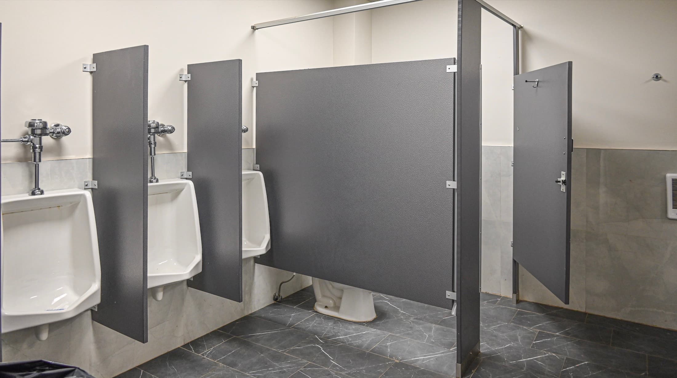 Washroom cubicles and urinals with dark tiled floor and full-height dividers