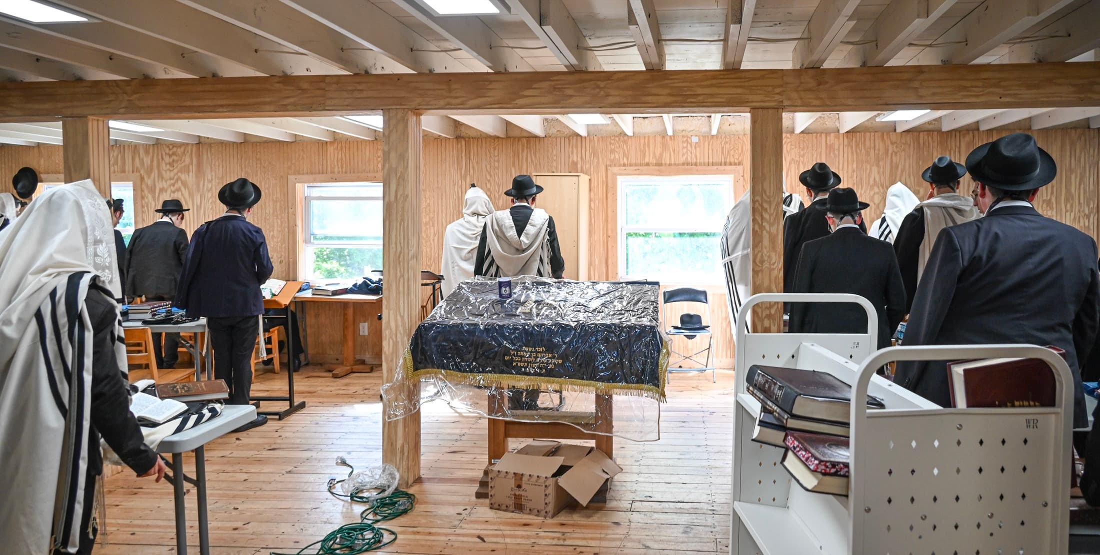 A timber-framed beis medrash in use, light coming in from windows along the wall